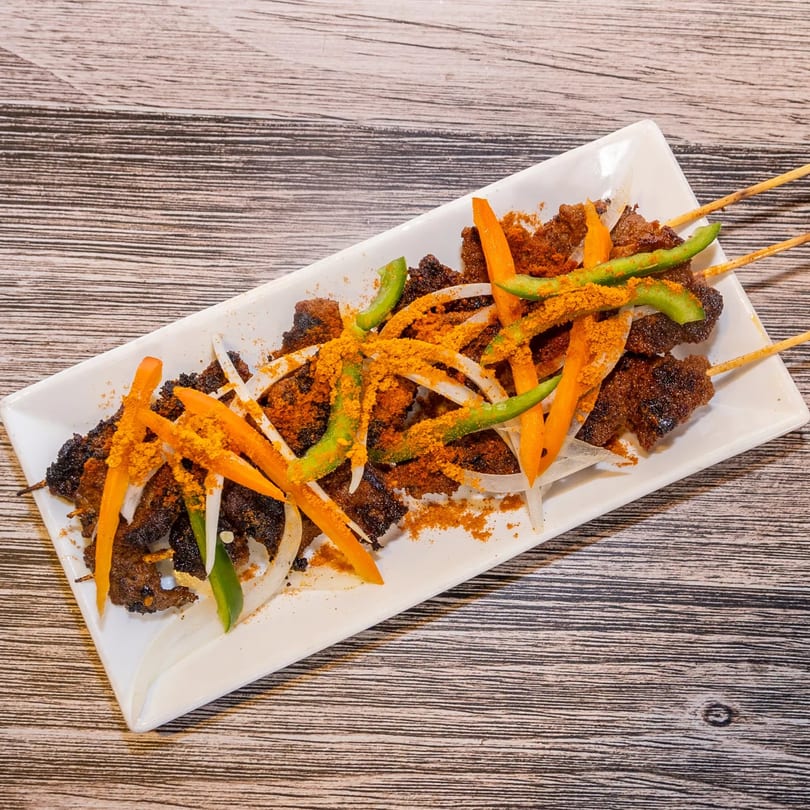 Dalia's African Cuisine suya skewers with onions, bell peppers, and spices on a white plate.