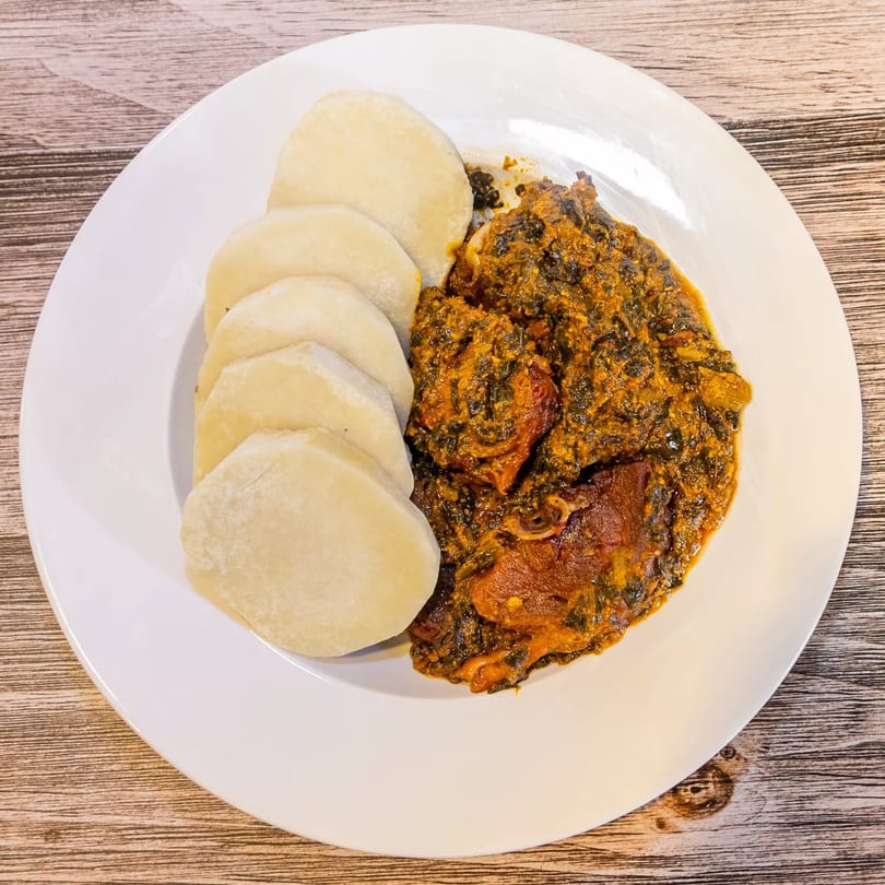 A white plate of Dalia's African Cuisine with fufu and a rich, dark stew.