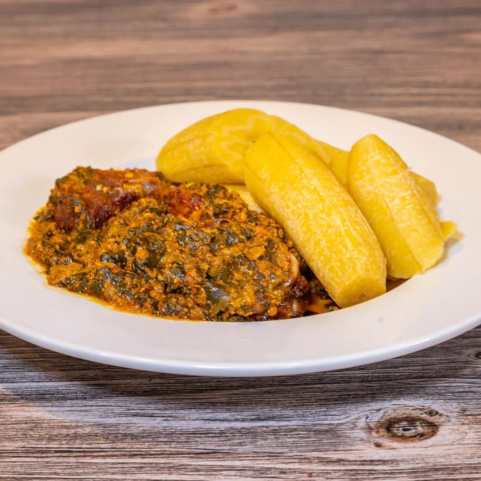 Dalia's African Cuisine dish with green stew, meat, and yellow plantains on a white plate.