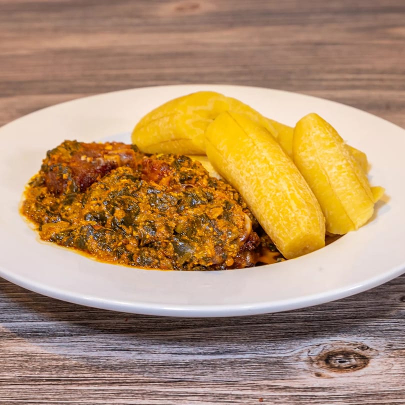 Dalia's African Cuisine dish with green stew, meat, and yellow plantains on a white plate.